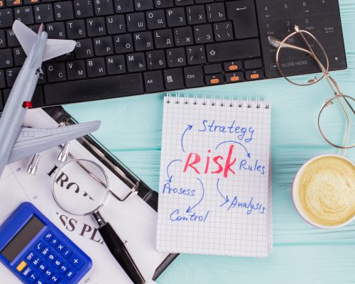 Office desk with stuff and note about risk. Airplane, calculator, cup of coffee on wooden table.