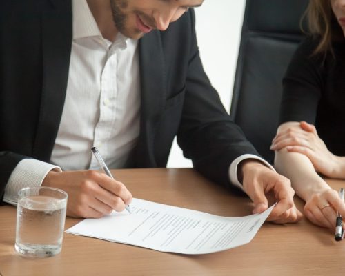Satisfied smiling businessman in suit signing contract at meeting concept, investor or entrepreneur putting written signature on business document making good partnership deal, taking loan insurance